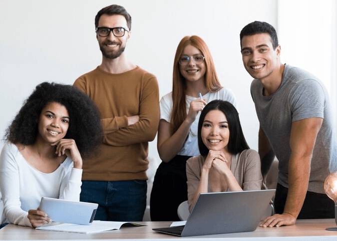 5 pessoas sorridentes trabalhando, 3 estão em pé e 2 sentadas.